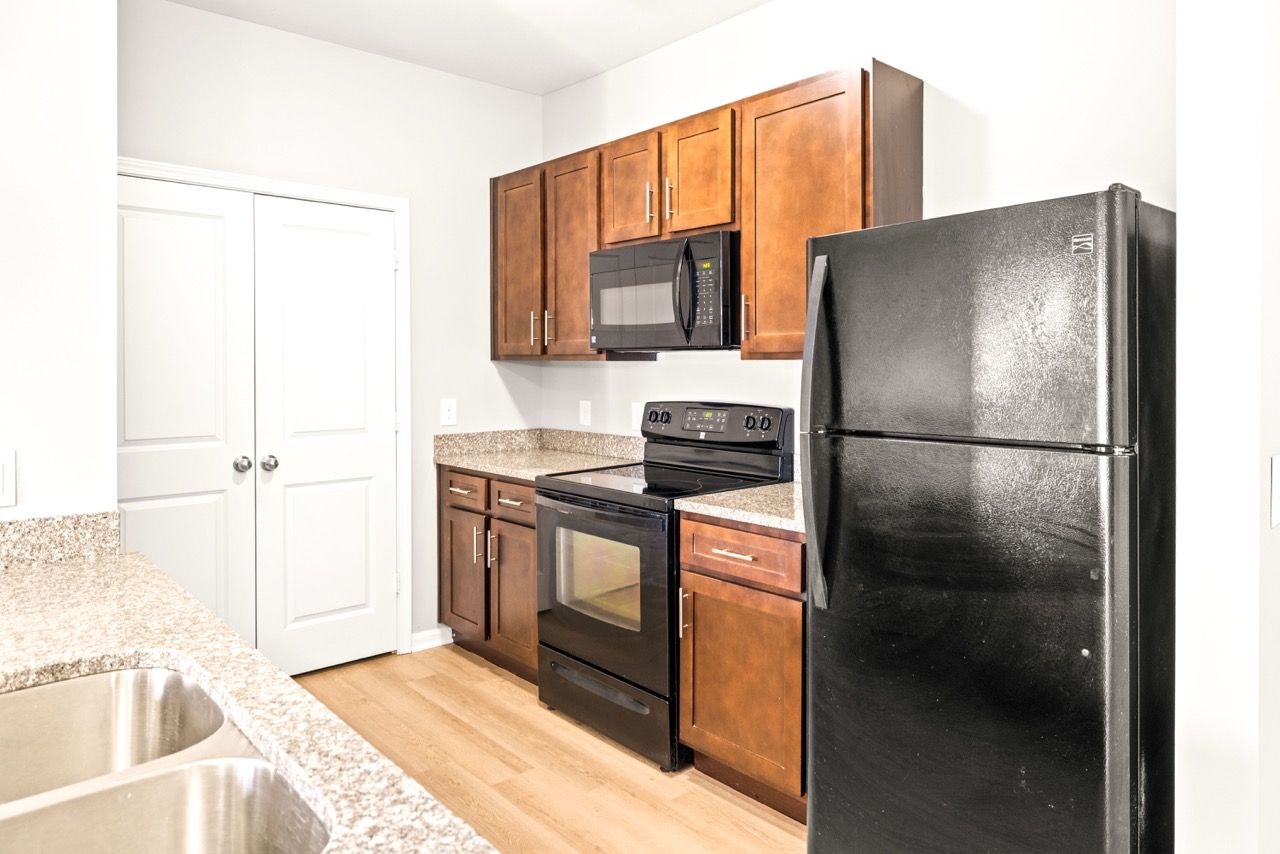 Kitchen in an apartment with granite counters, dark wood cabinets, and black appliances.