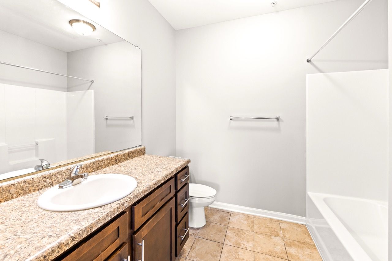 Bathroom with granite countertop, single sink, dark wood vanity, toilet, and bathtub.