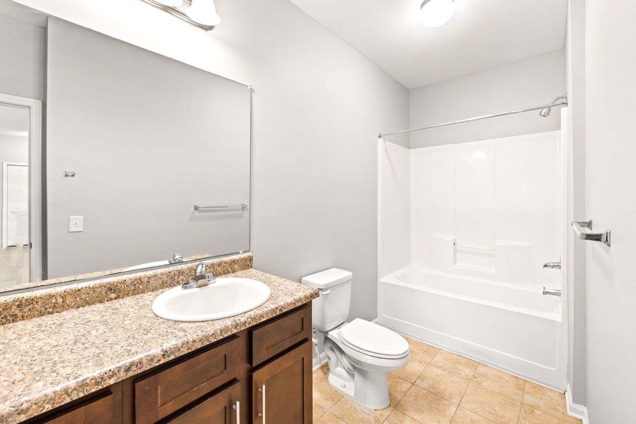 Bathroom featuring granite countertop, single-sink vanity, toilet, and white tub/shower.
