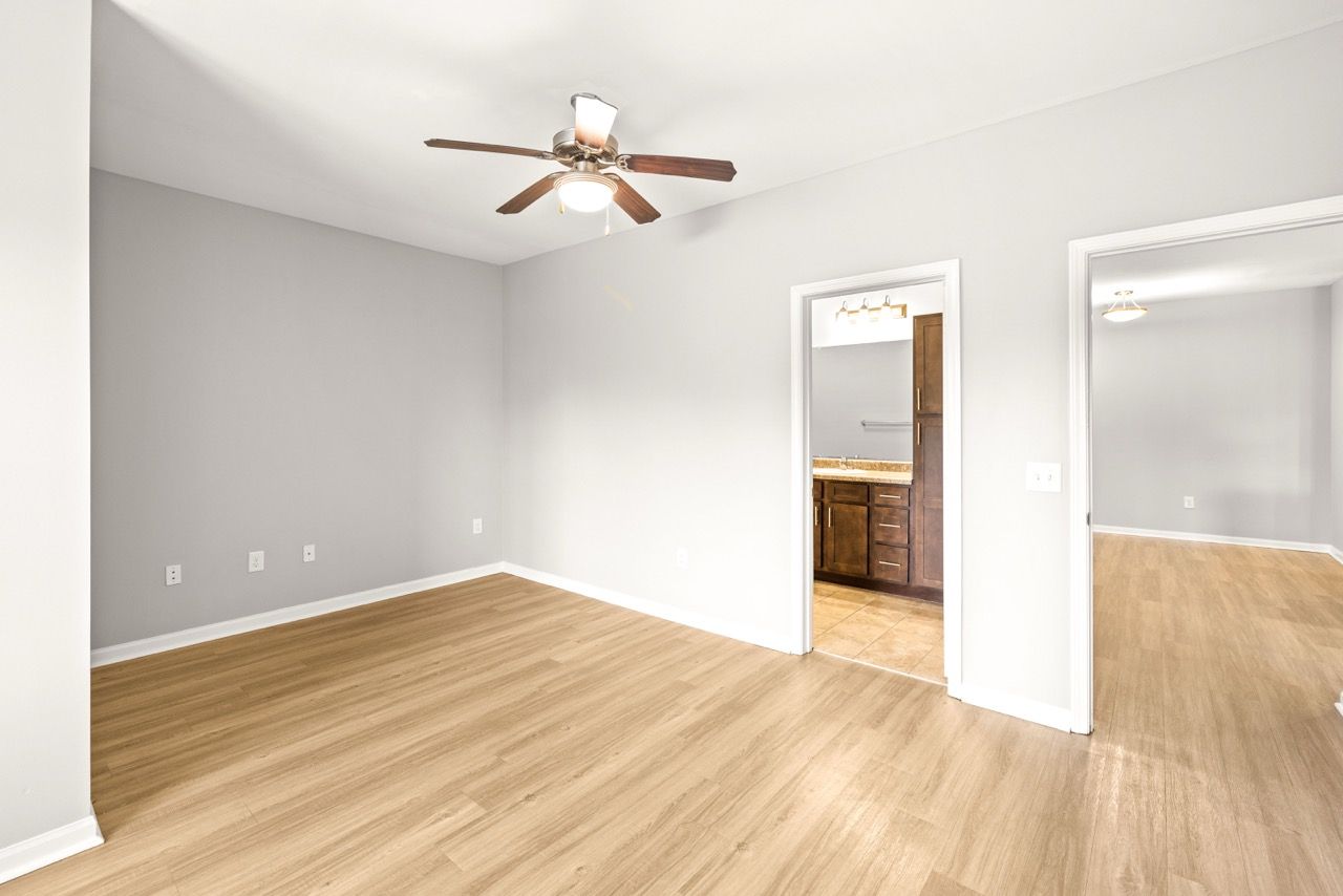 Empty living area with wood-look flooring, gray walls, and a ceiling fan.