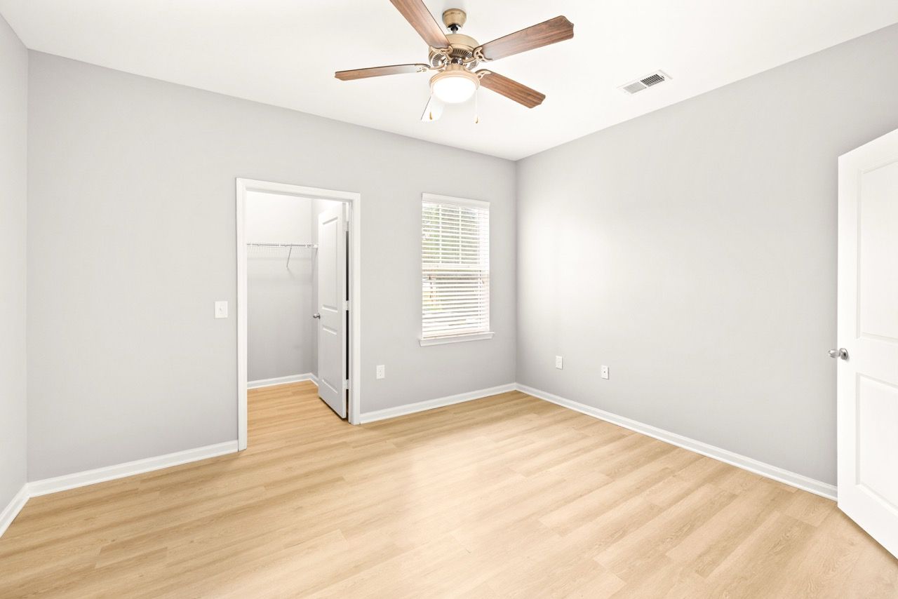 Empty bedroom with gray walls, wood-look flooring, ceiling fan, a window with blinds, and a closet.