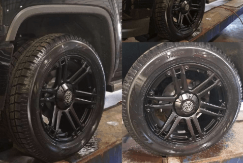 A black truck with black wheels and tires is sitting on a lift.