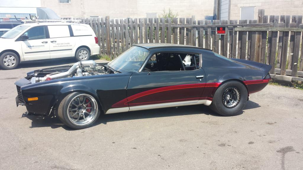 A black and red car is parked in front of a wooden fence.