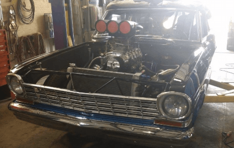 A blue car with a big engine is parked in a garage.