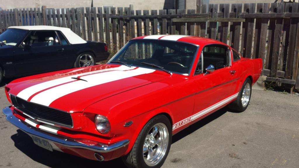 A red mustang with white stripes is parked in front of a wooden fence