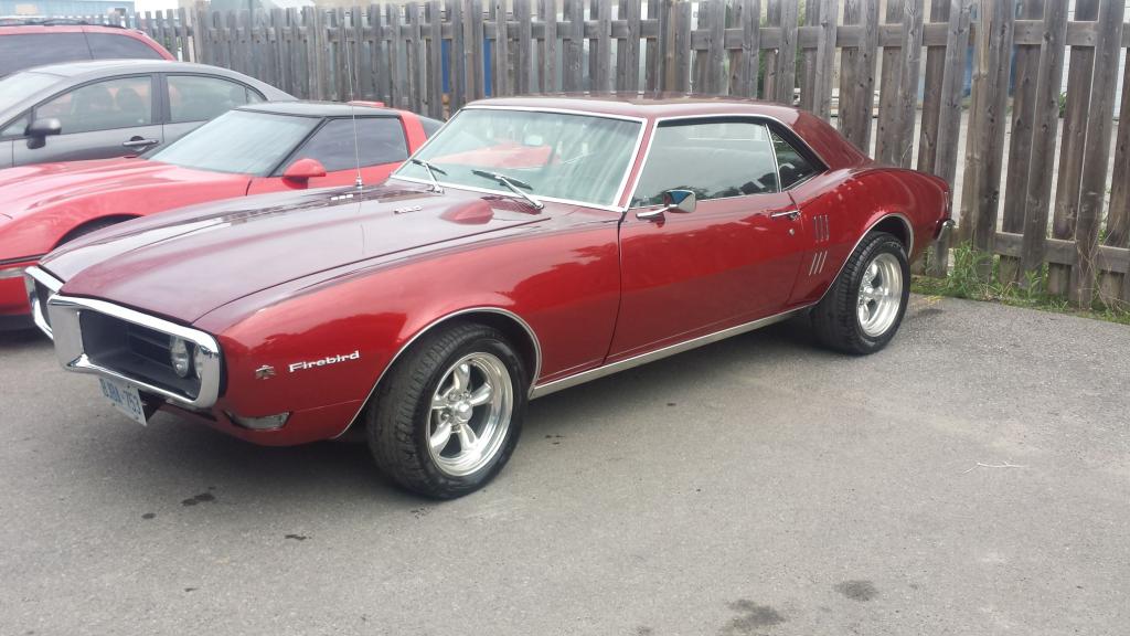 A red pontiac firebird is parked in front of a wooden fence.
