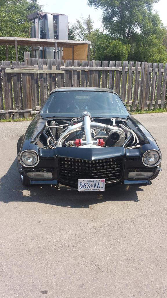 A black car with the hood up is parked in front of a wooden fence