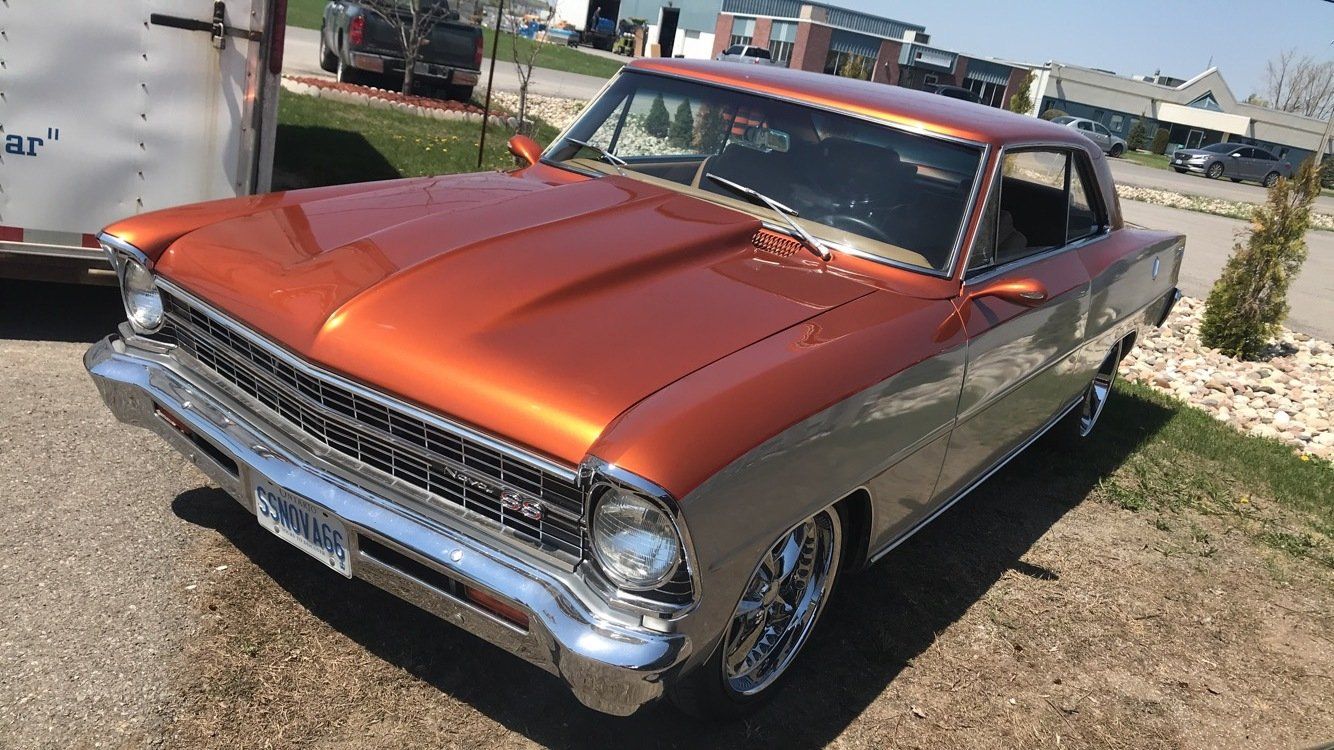 An orange car is parked in a parking lot next to a trailer.