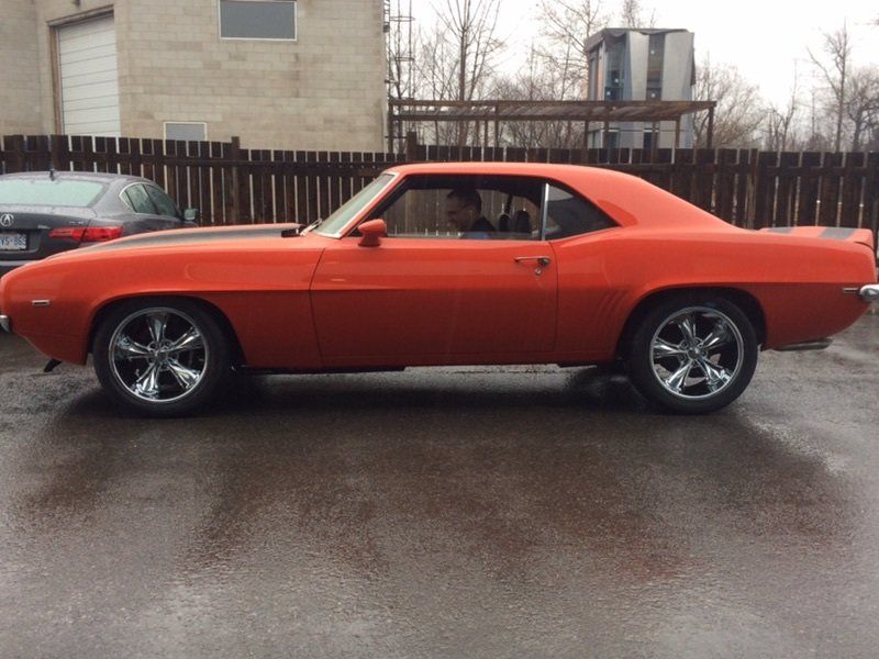 An orange car with chrome wheels is parked in a parking lot