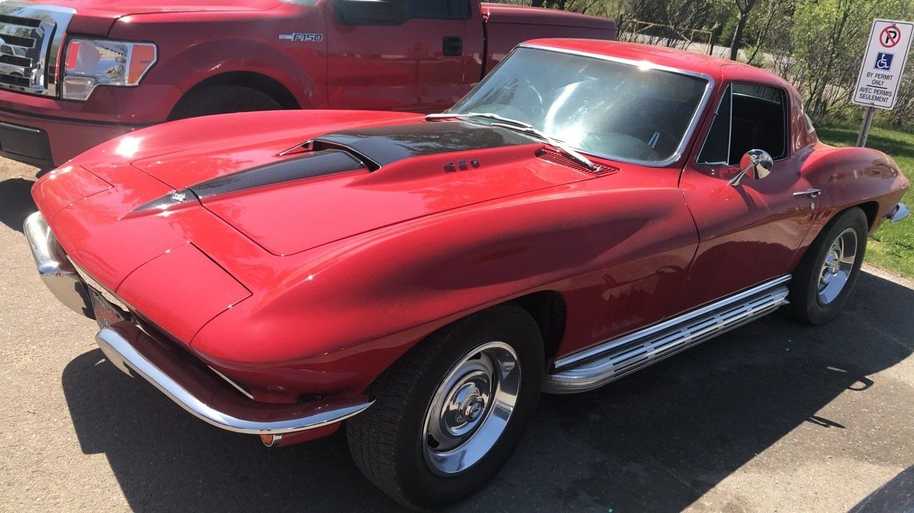 A red corvette is parked in a parking lot next to a red truck.