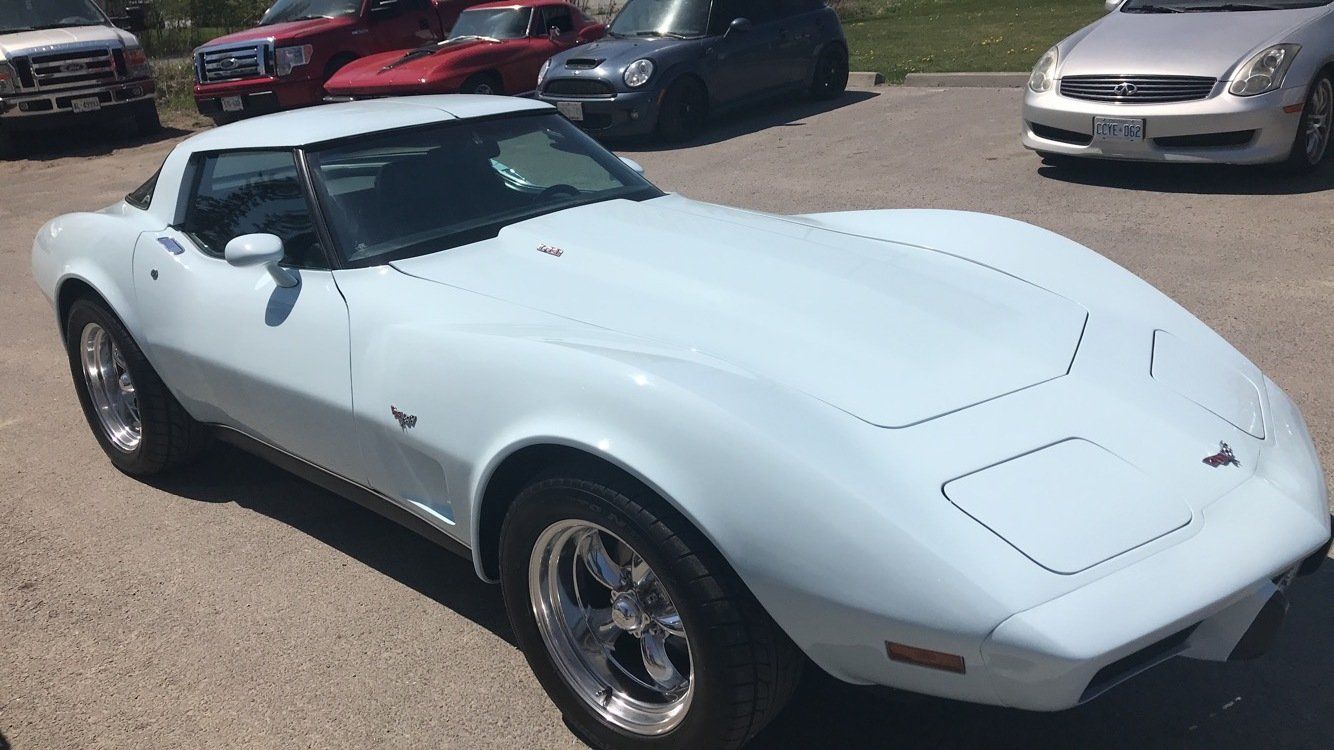 A white corvette is parked in a parking lot next to other cars.