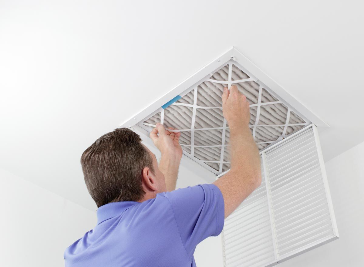 A man is installing a filter on a ceiling vent.