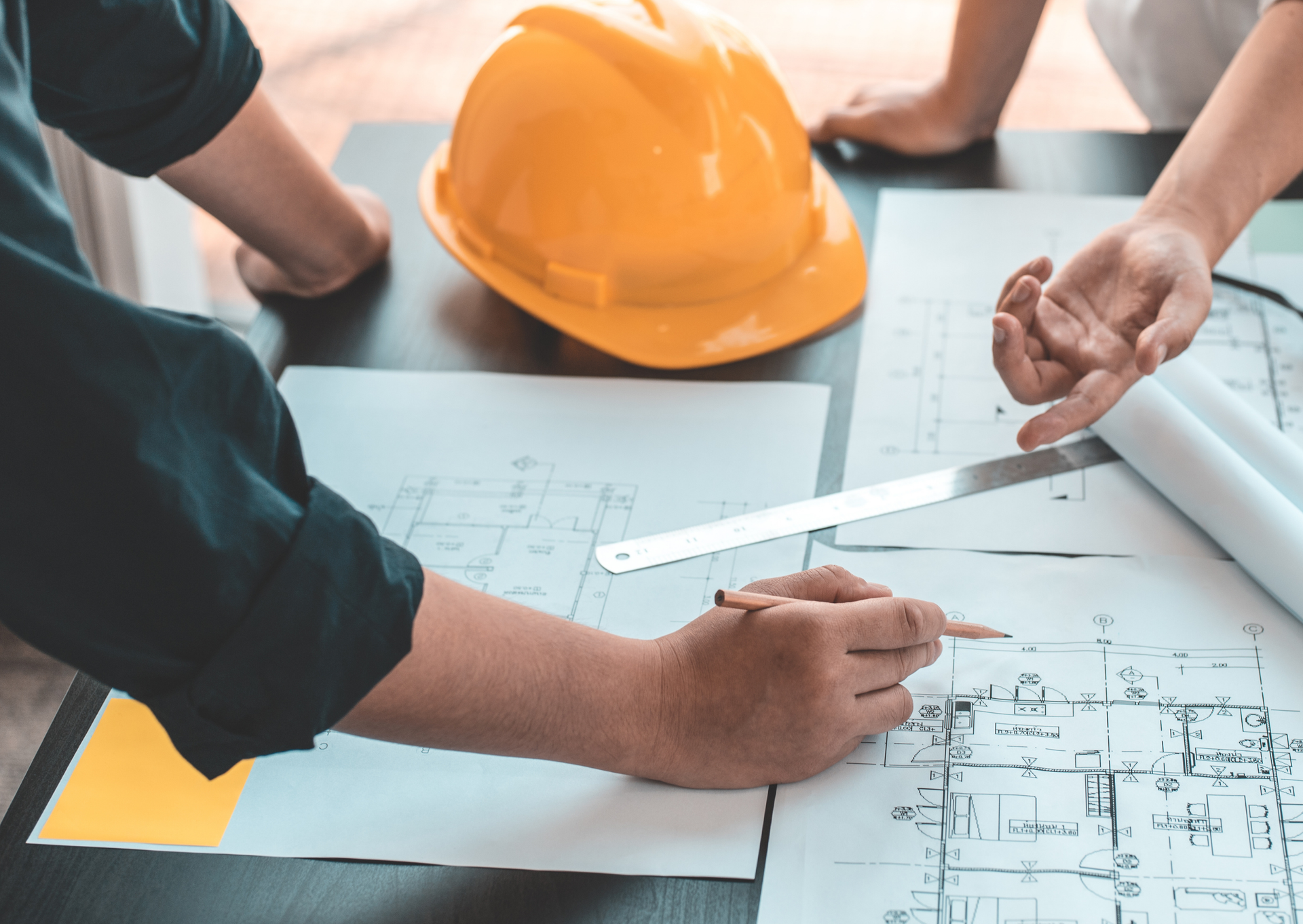 Architects reviewing blueprints, a yellow hard hat, and a ruler on a table.