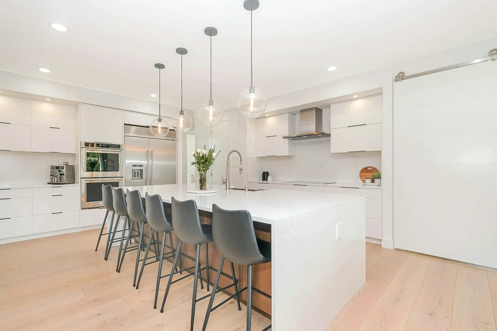 White modern kitchen with large island and seating, overhead lights, and stainless steel appliances.