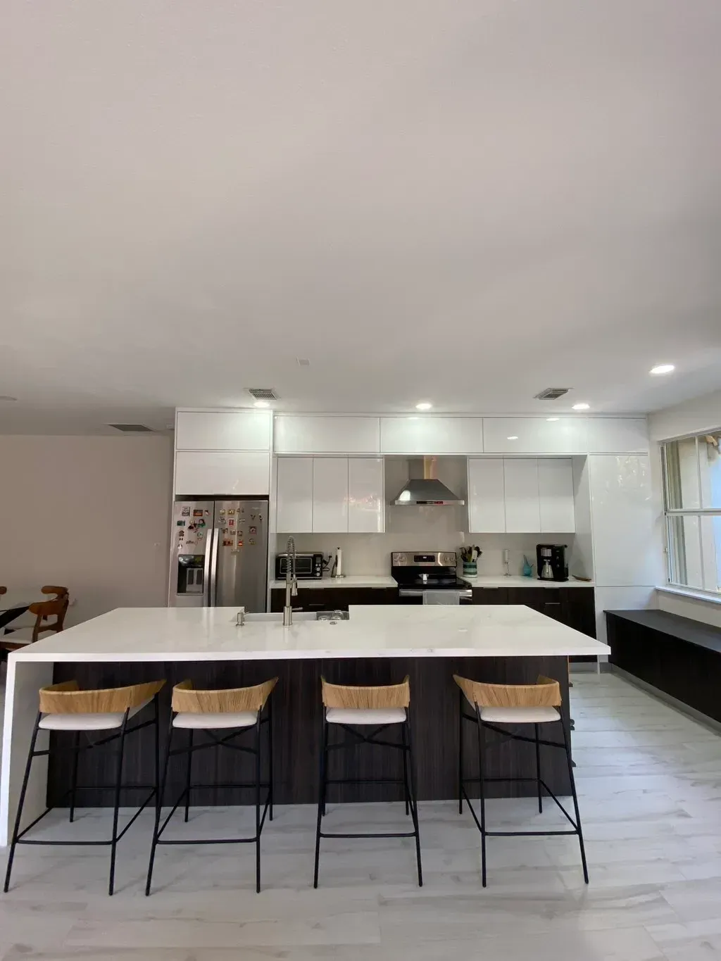 Modern kitchen with an island and bar stools, white cabinets, and a stainless steel refrigerator.