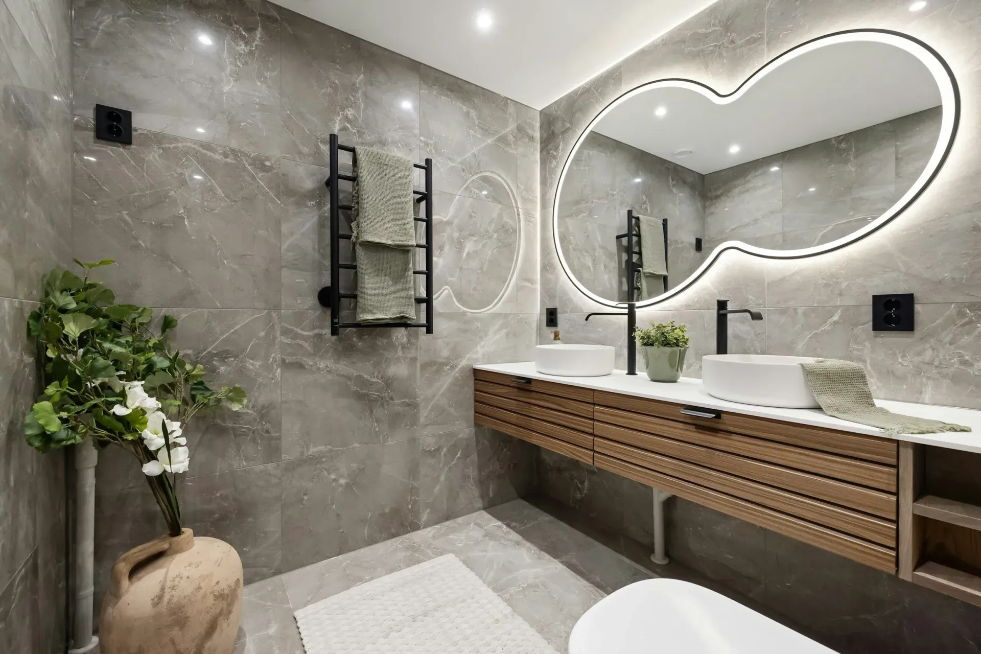 Modern bathroom with gray marble tile, floating wood vanity, unique mirror, and greenery.