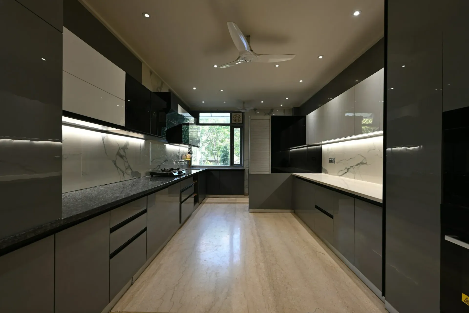Modern gray kitchen with glossy cabinets, marble backsplash, and light wood floor.