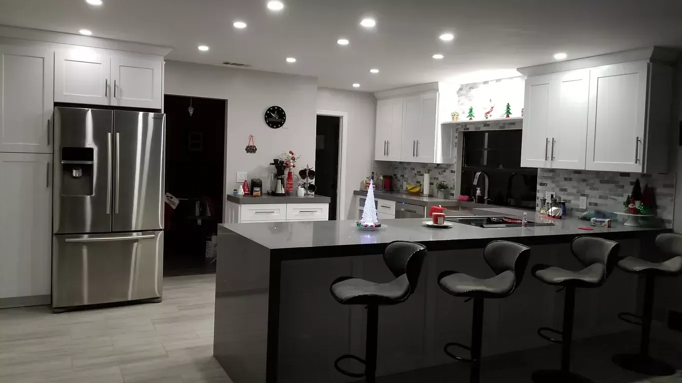 Kitchen with white cabinets, stainless steel fridge, gray island with bar stools, and overhead lighting.