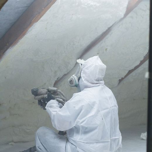 A man in a white suit is spraying foam on a wall