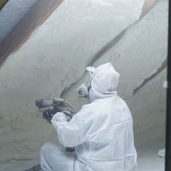 A man in a white suit is spraying foam on a wall