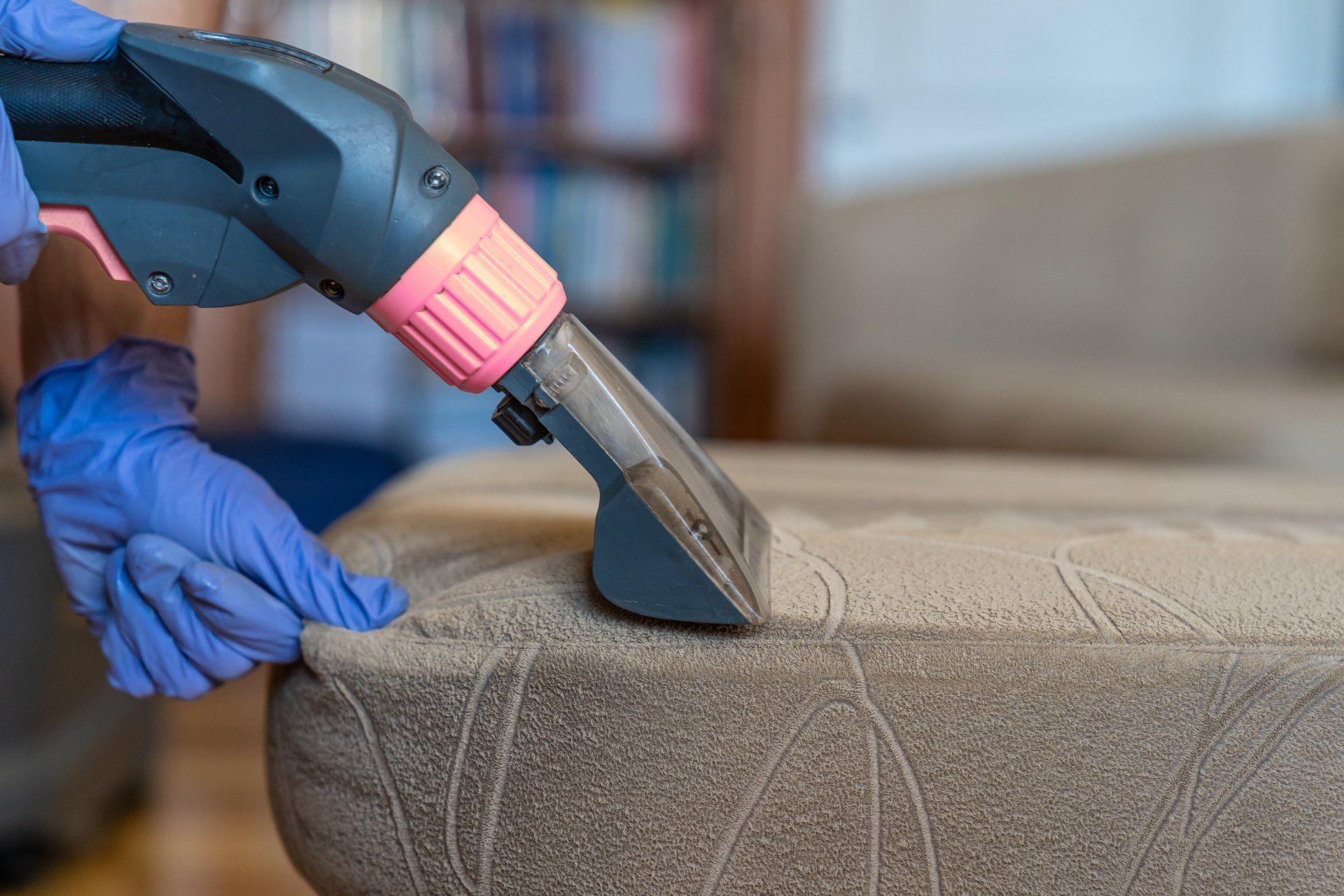 A person is cleaning a couch with a vacuum cleaner.