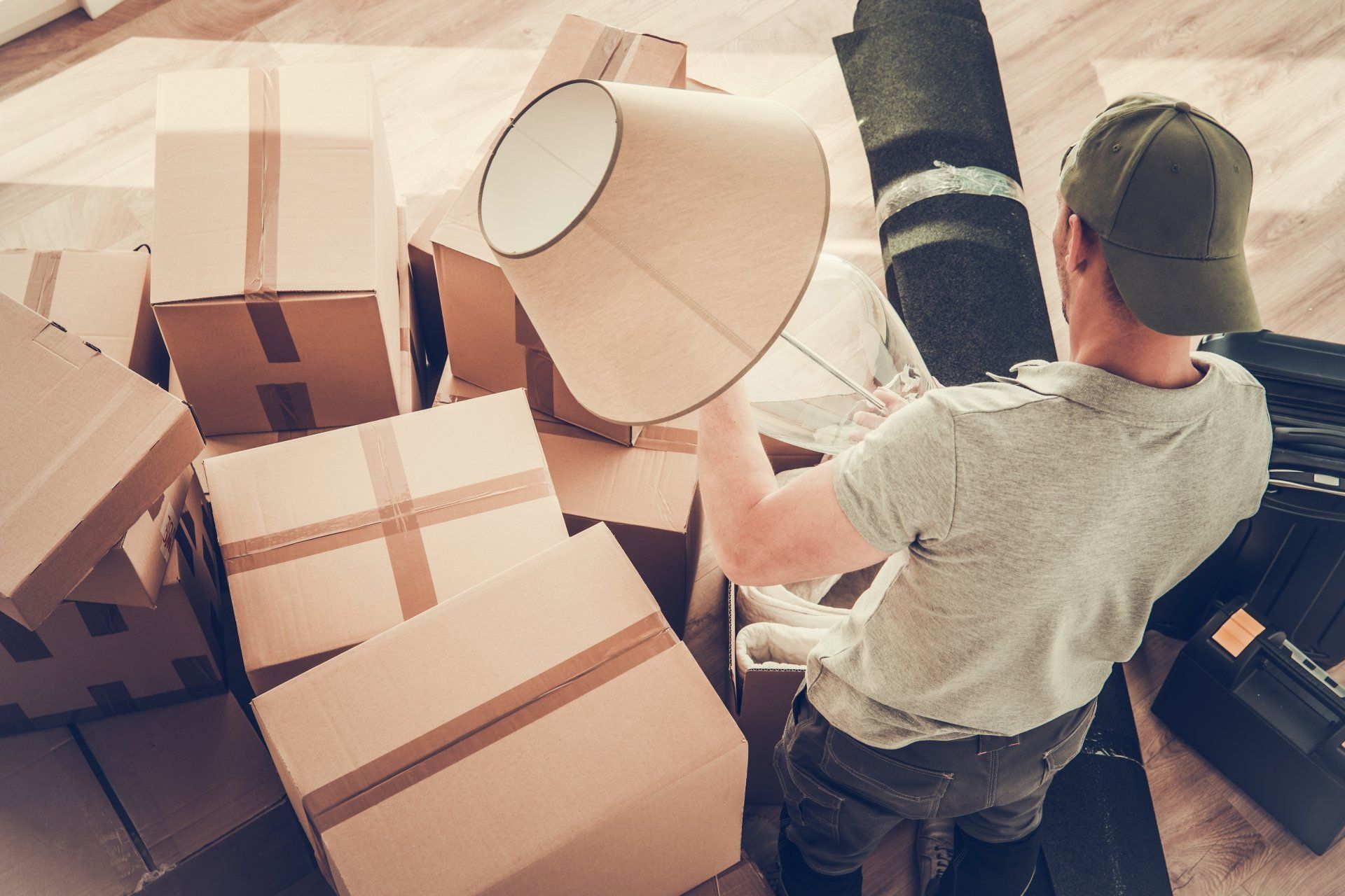A man is holding a lamp shade in front of a pile of cardboard boxes.