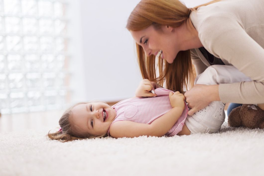 A woman is playing with a baby girl on the floor.