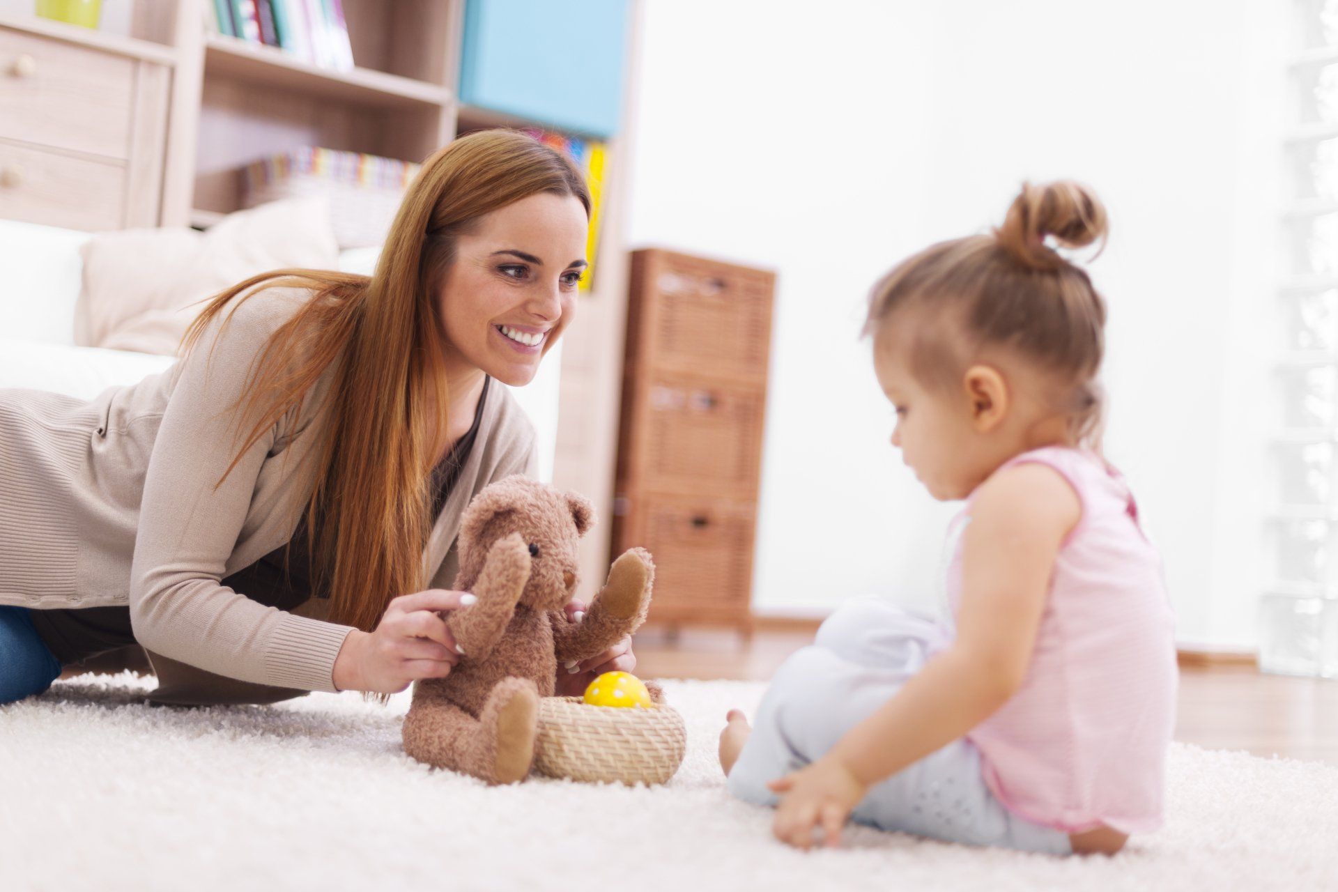 A woman and a little girl are playing with stuffed animals on the floor.