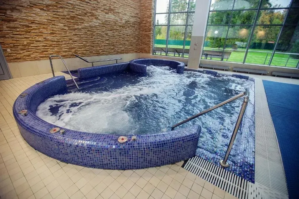 A tiled, circular whirlpool spa with bubbling jets, set in a room with a textured stone wall and large windows.