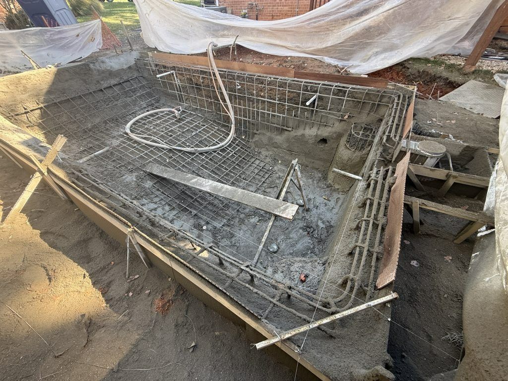 A half-finished rectangular swimming pool construction site with steel rebar framing and concrete layers in a yard.