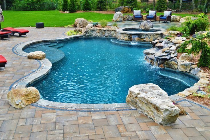 A freeform swimming pool with a stone waterfall, hot tub, and patio area in a landscaped backyard.