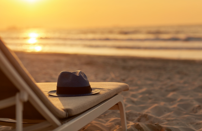 A hat is sitting on a beach chair at sunset.