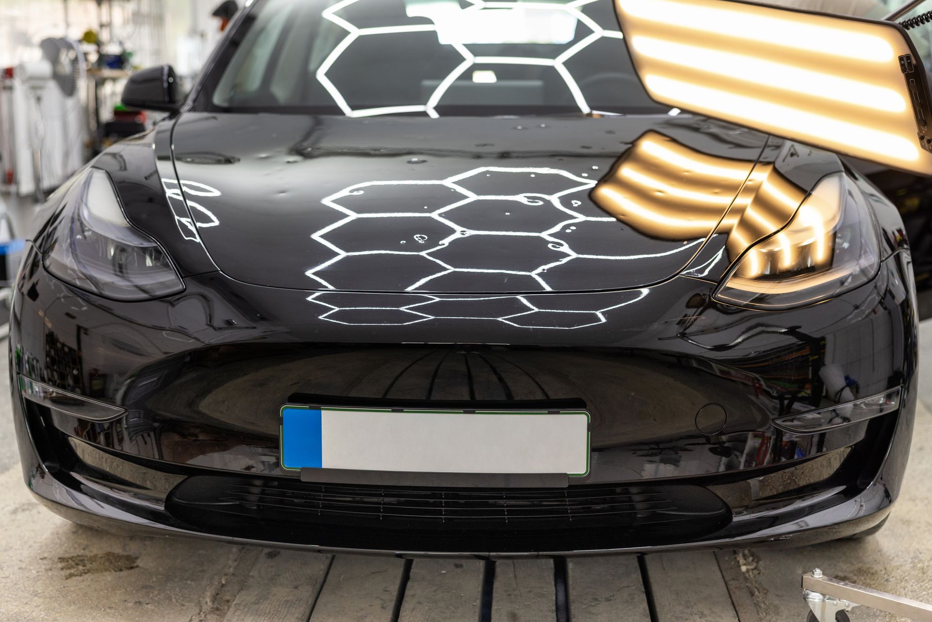 Black electric car front view in a showroom, with bright reflections on the hood and windshield