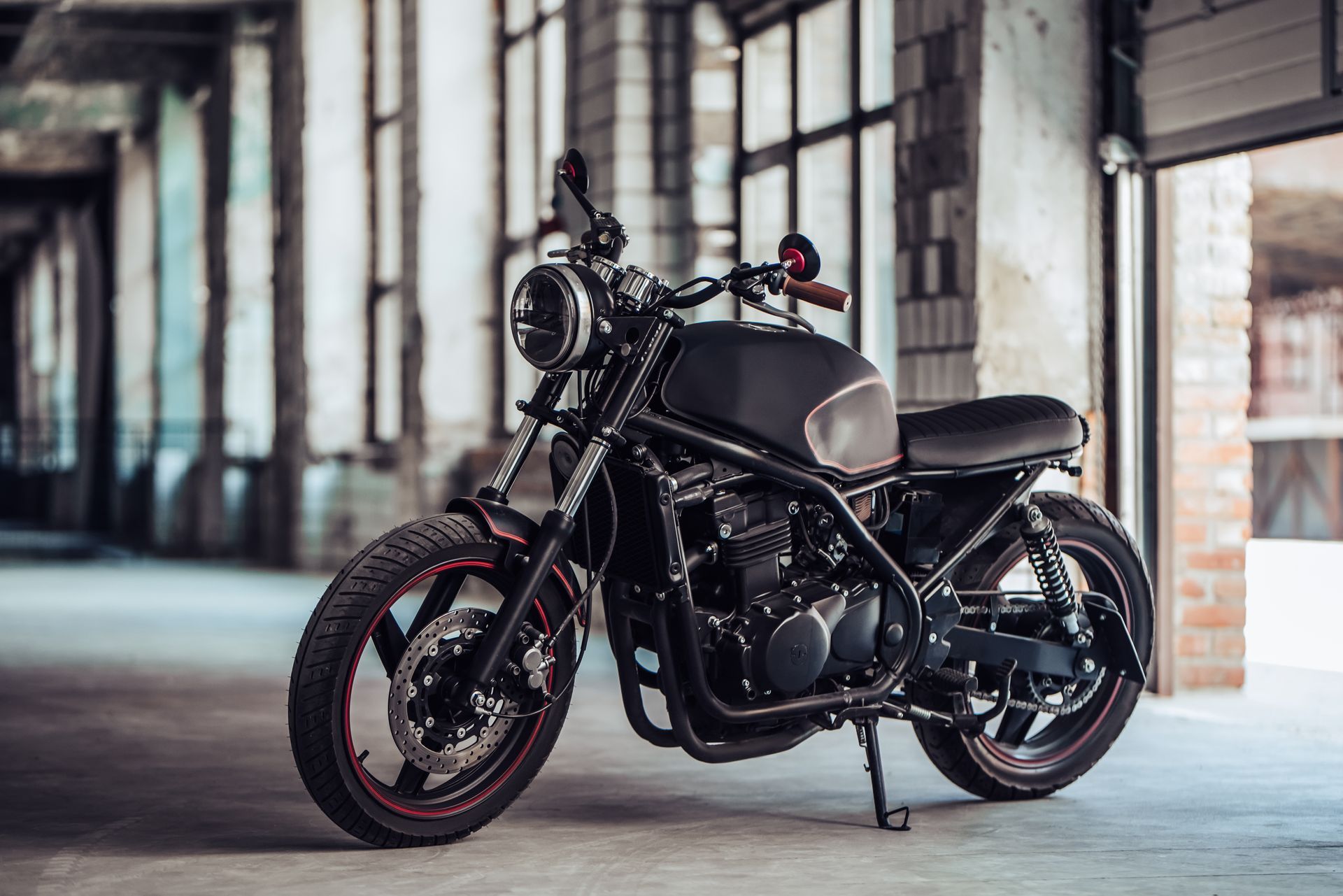Black custom motorcycle parked in an industrial warehouse with brick walls and concrete floor