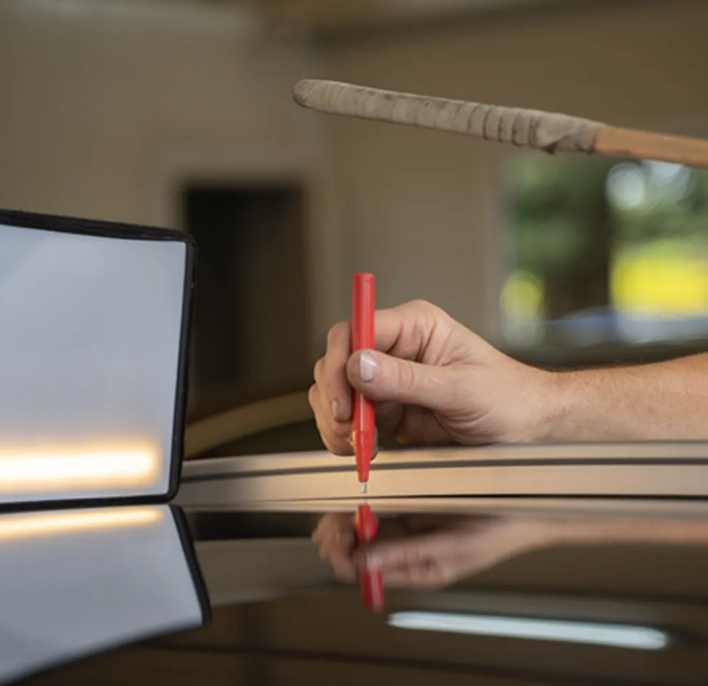 Hand holding a red pen over a glossy table with a blurred laptop in the background