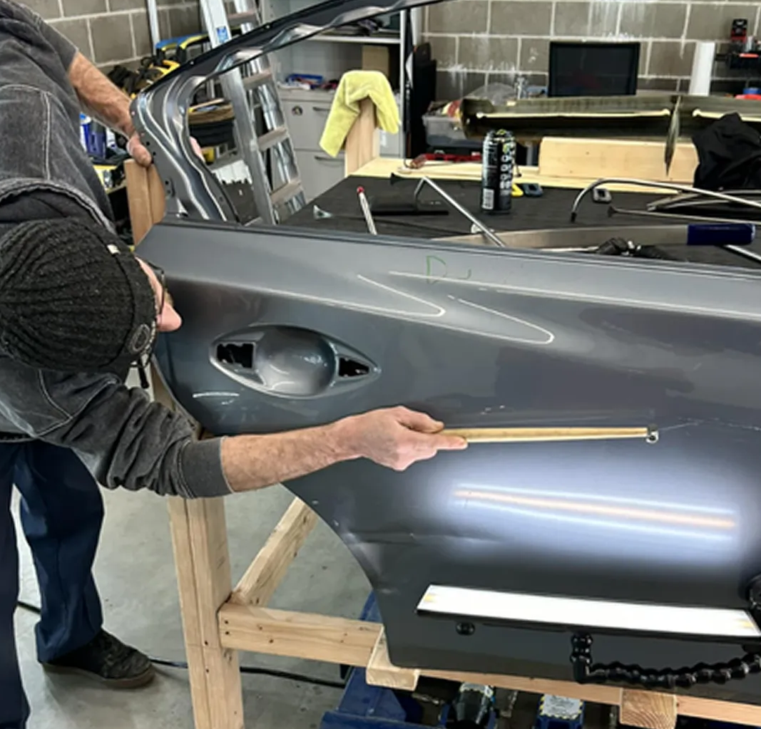 Person sanding a gray car body panel in a workshop