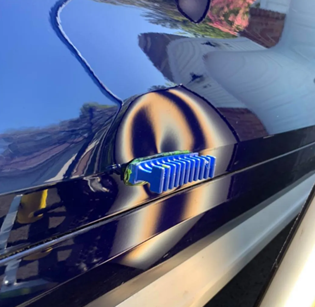 Close-up of a glossy black car door with a blue-and-yellow striped handle reflecting surroundings