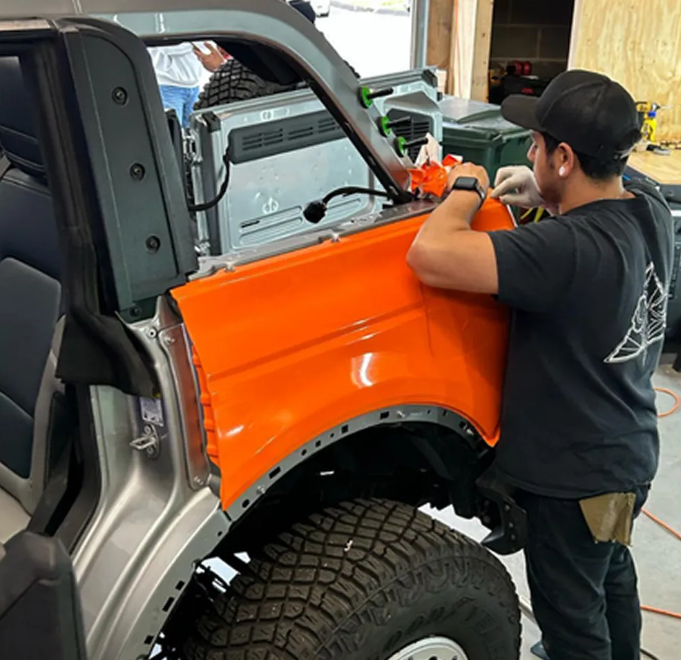 Mechanic applying orange wrap to a truck fender in a garage.