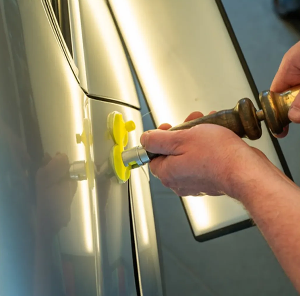 Hands using a suction-cup dent puller on a car door to remove a dent