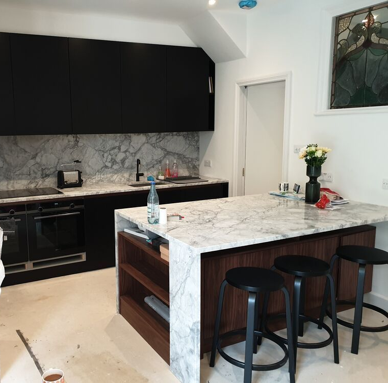 Modern kitchen with black cabinets, marble countertops, island with seating, and a stained-glass window.