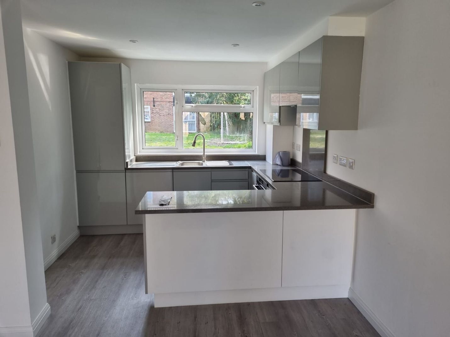 Gray and white modern kitchen with countertops, cabinets, and a window.