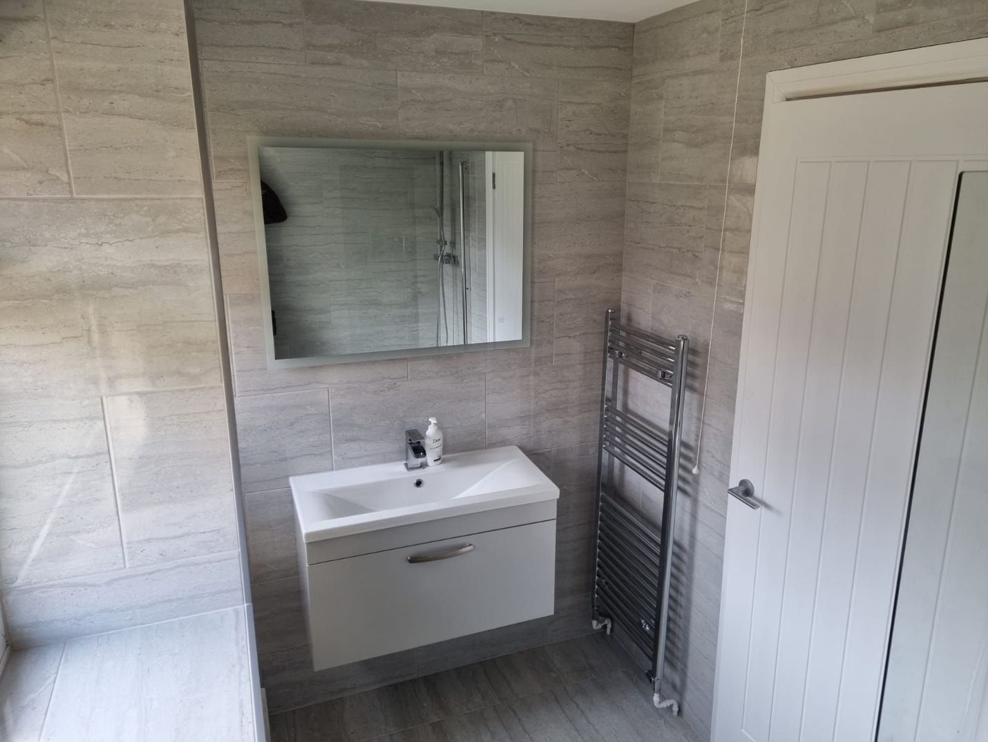 Modern bathroom with gray tiled walls, floating white vanity, mirror, and towel rack.