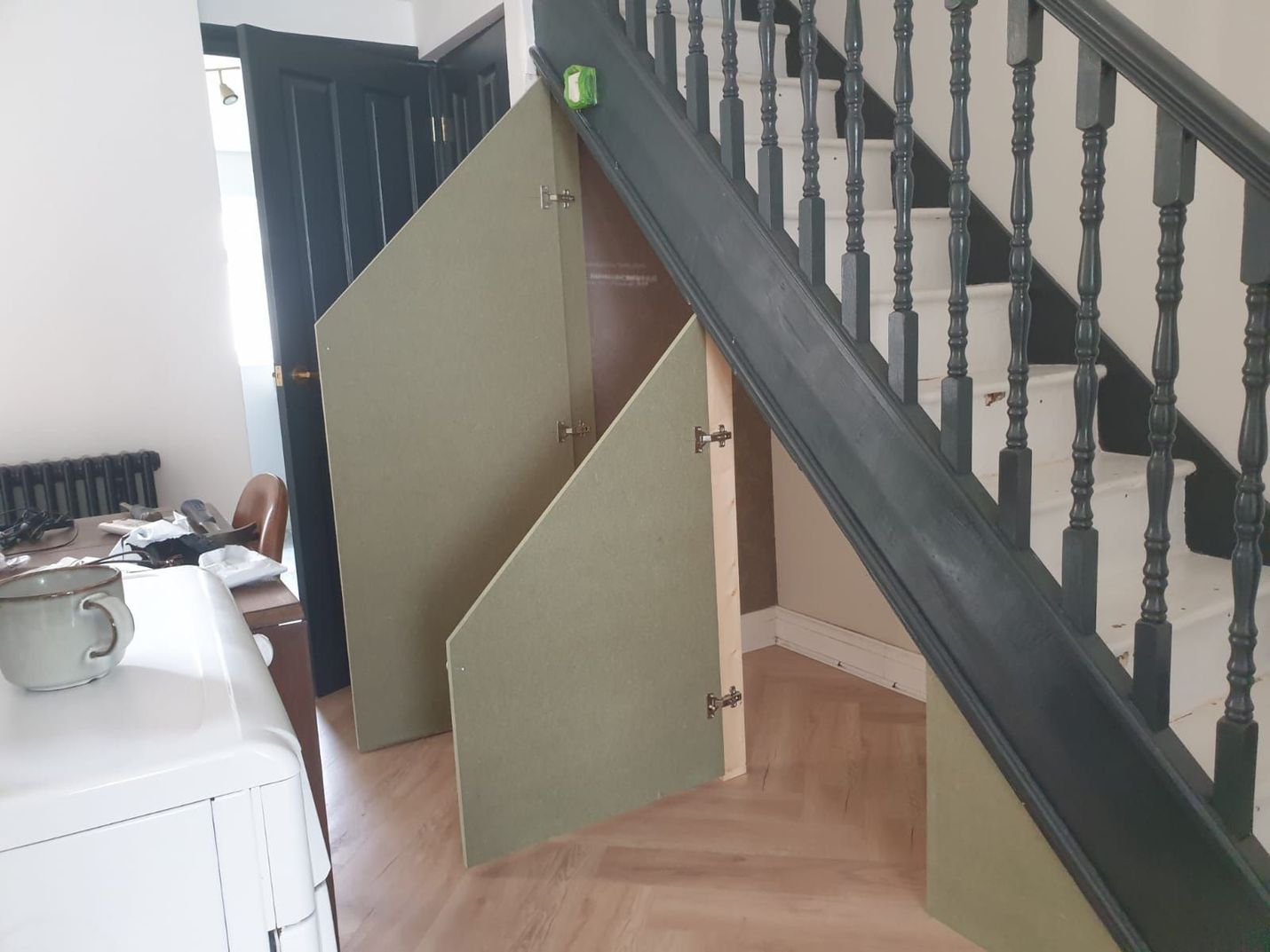 Wooden under-stair storage with open green doors, staircase with dark green railing.