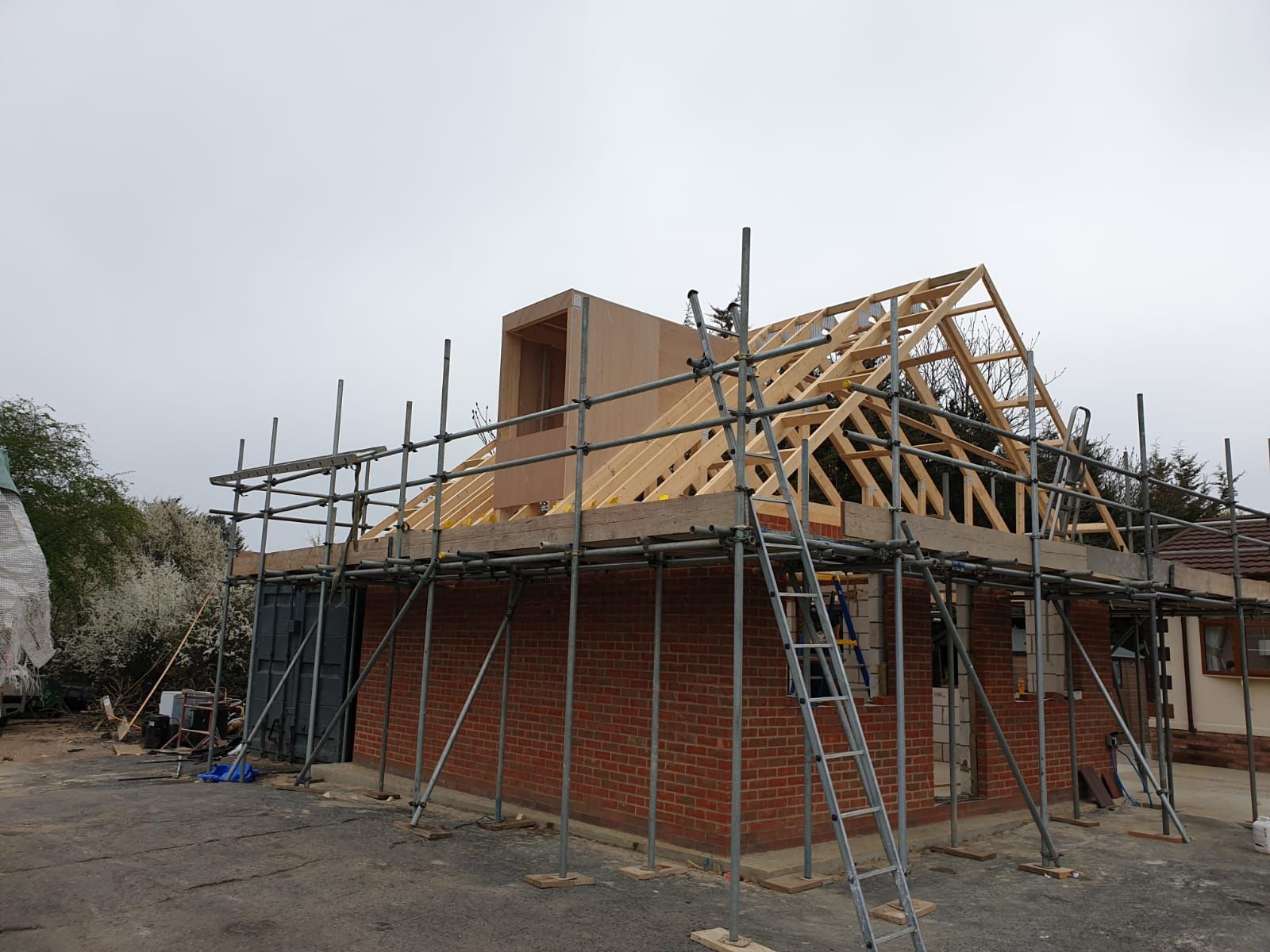 Building under construction: brick structure with roof trusses and scaffolding.