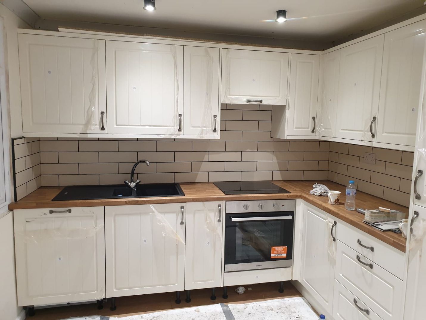 Off-white kitchen cabinets and brick backsplash, wooden countertops, black appliances, and a stainless steel faucet.