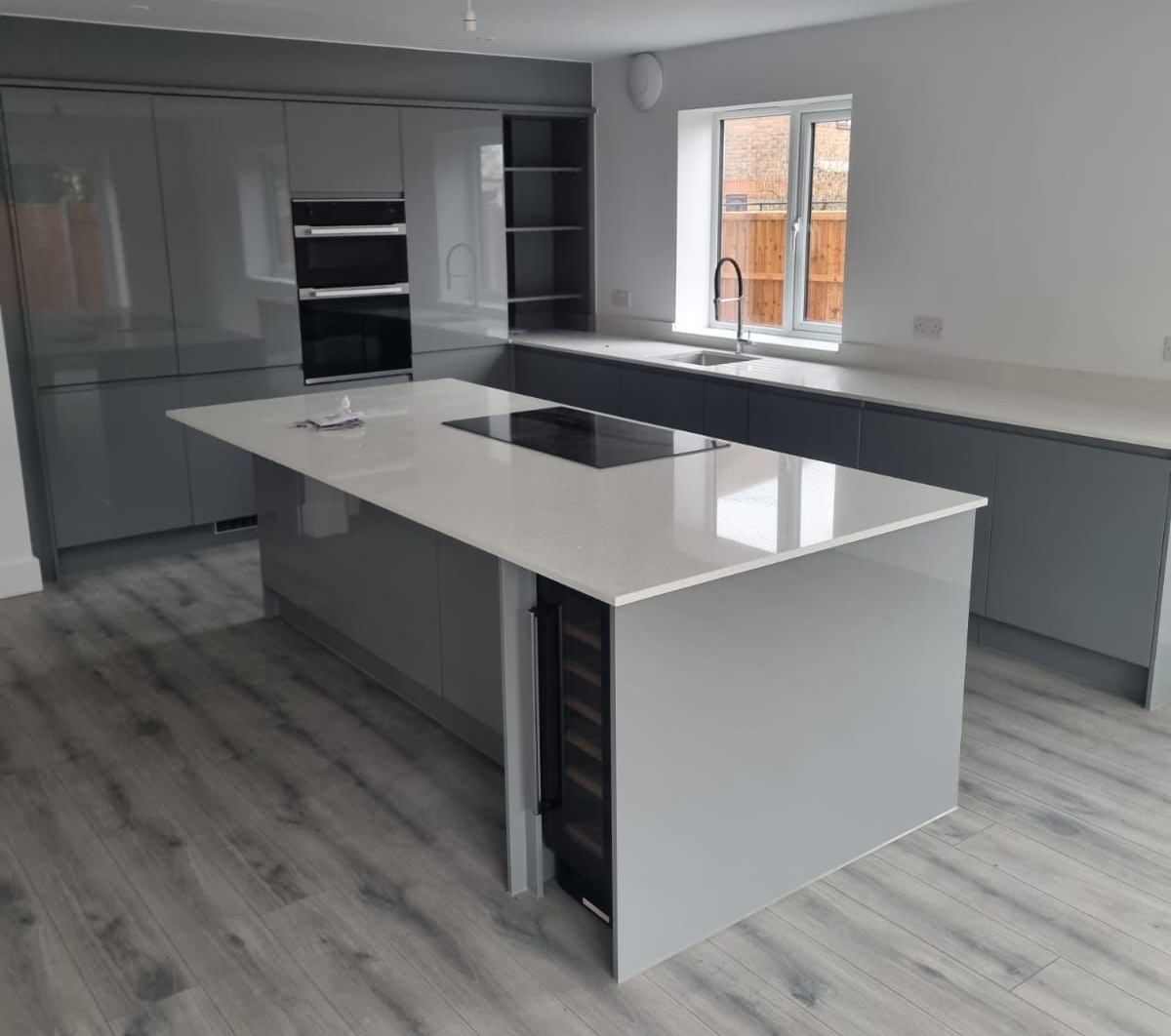 Modern gray kitchen with island, white countertop, built-in cooktop and wine cooler, light wood flooring.