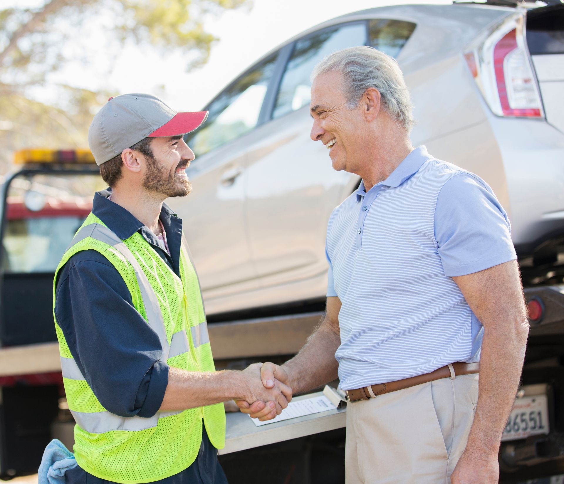 two men are shaking hands in front of a tow truck .