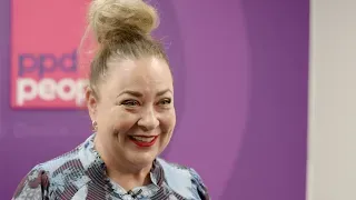 Woman with blonde bun smiles, in front of purple backdrop.  PPD People logo visible.