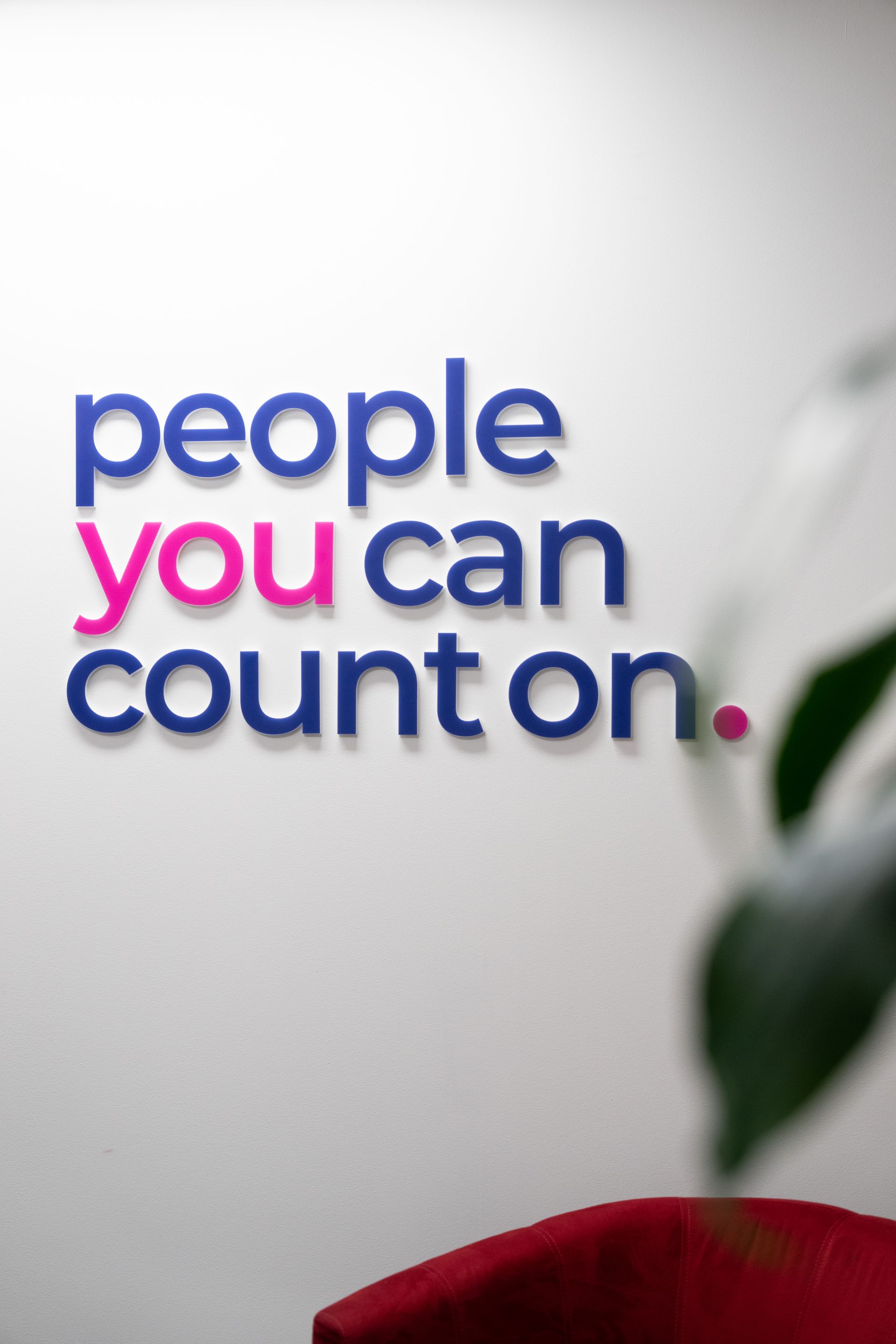 Woman with dark hair looks at document at desk, presumably in office. Blue, patterned shirt.