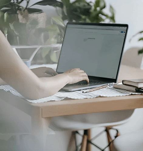 Overhead view: Person using laptop at desk with photo frames, notebook, phone, and stack of paper.